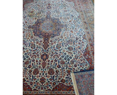 A large Kashan rug, Central Persia, the central blue lozenge on a floral ivory field with claret borders decorated with flowe