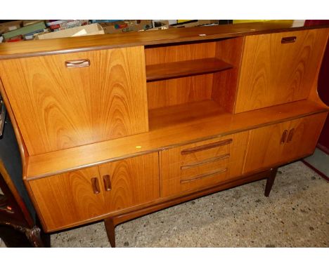 A 1970s G-Plan teak side cabinet, the raised back with fall front compartment, sliding door, open shelf over three drawers to