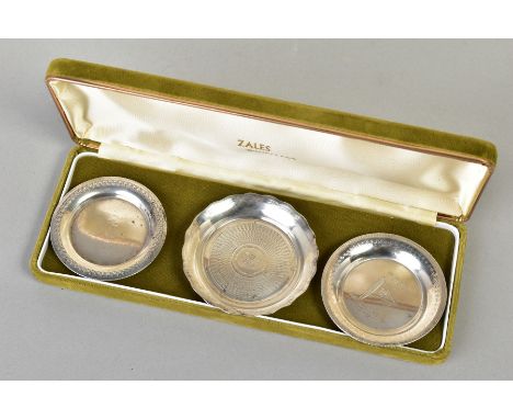THREE SMALL WHITE METAIL DISHES, to include a small floral embossed rim dish, an engine turn design dish engraved 'A.S.C 1949