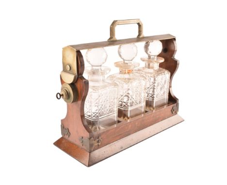 A three decanter wooden tantalus with metal handle and fixings, complete with three cut glass decanters and a key.