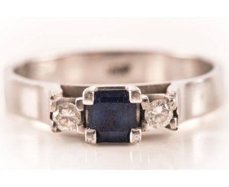 An 18 carat white gold sapphire and diamond three stone ring, set to centre with a square step cut sapphire with an approxima