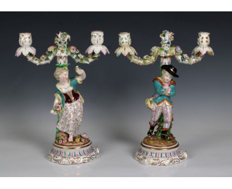 A pair of Continental porcelain twin branched candelabra, featuring a boy and girl, applied flowers, polychrome and gilded de