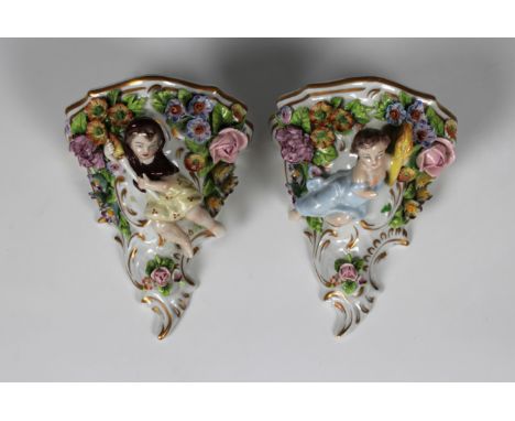 Pair of Sitzendorf, Germany, porcelain wall brackets, each featuring young children holding torches, decorated with applied p