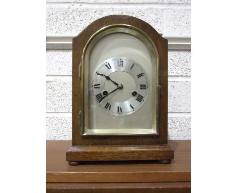 An early-20th century oak-cased arched mantel clock, with silvered dial and gong-striking movement, labelled From Morath Bros