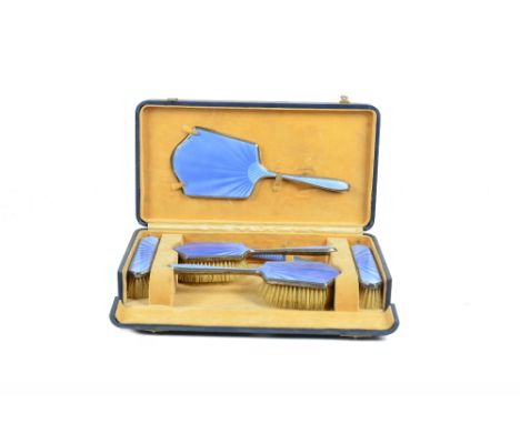 A cased six piece dressing table set, with blue enamel engine turned decoration and silver backs, hall marked Albert Carter, 