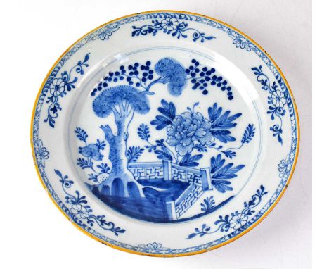 A late 18th century Delftware blue and white charger, painted in the chinoiserie style, with peonies and trees within a flora