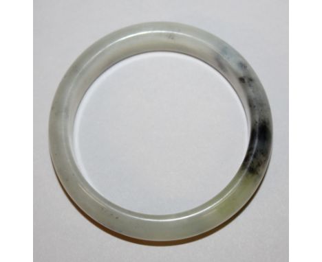 A CHINESE JADE-LIKE BANGLE, the pale body with grey and black inclusions, 2.9in diameter, the inner rim 2.3in diameter.