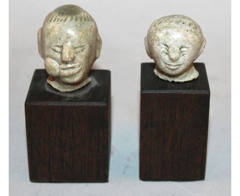 TWO SIMILAR SAWANKHALOK CELADON GLAZED CERAMIC HEADS OF THE BOY BUDDHA, 14th/16th Century, each mounted on a wood plinth, the