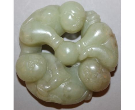 A CHINESE CELADON JADE LIKE PIERCED ROUNDEL OF THREE BOYS, playing with a ball, 2.2in diameter.