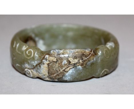 A CHINESE JADE BANGLE, carved in an archaic style with opposing dragons heads, 2.7in diameter, the inner rim 2.2in diameter.