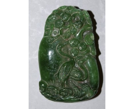 A CHINESE APPLE-GREEN JADE-LIKE PENDANT, decorated with a pair of storks standing beside a large vase of flowers, 2.1in high.