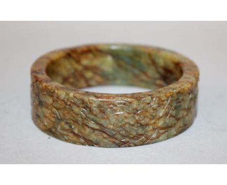 AN UNUSUAL CHINESE JADE BANGLE, 19th Century or earlier, the stone of underlying green tone with dense brown and russet stria