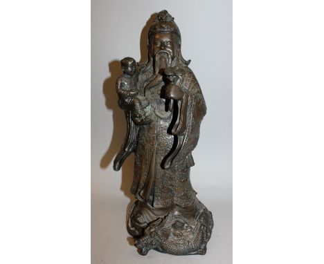 A CHINESE BRONZE FIGURE OF AN IMMORTAL, clad in cloud decorated robes, holding a child in one hand and a ruyi sceptre in the 