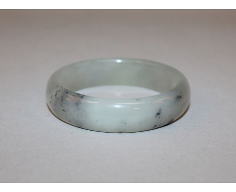 A CHINESE JADE-LIKE BANGLE, the grey stone with darker flecks, 2.9in diameter, the inner rim 2.3in diameter.