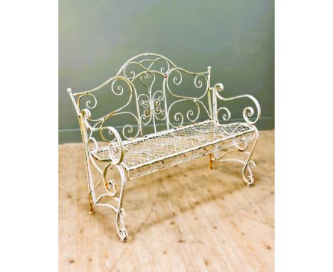 An arched back garden bench, overpainted in white with a screoll back design above a lattice work seat, standing on scroll en