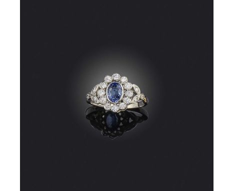 A sapphire and diamond cluster ring, the oval sapphire set within a surround of round brilliant-cut diamonds and bifurcated d