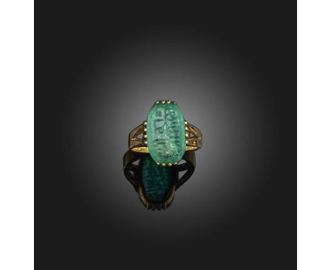 A carved emerald ring, set with an elongated octagonal emerald measuring 15.1 x 9.4 x 4.0mm, its table engraved with an inscr