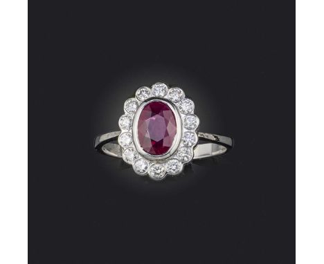 A ruby and diamond cluster ring, the oval-shaped ruby set within a surround of round brilliant-cut diamonds in 18ct white gol