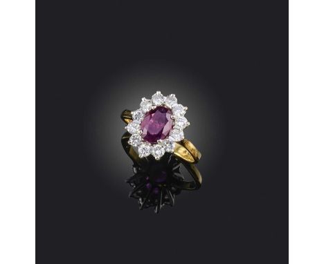 A ruby and diamond cluster ring, the oval-shaped ruby set within a surround of circular-cut diamonds in platinum and gold, Lo