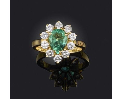 An emerald and diamond ring, of cluster design, claw-set with a pear-shaped emerald weighing approximately 1.00 carat, within