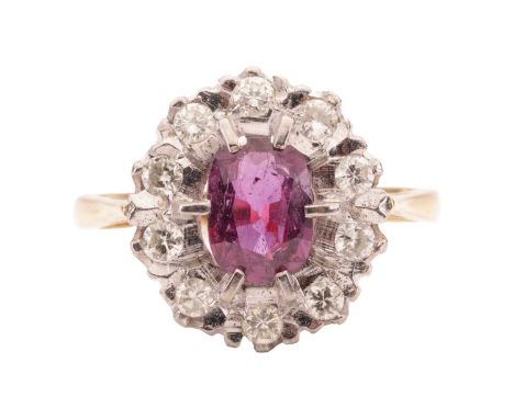 A ruby and diamond cluster ring. The central oval cut ruby measures 7.5mm x 5.4mm x 3mm, is surrounded by round brilliant dia
