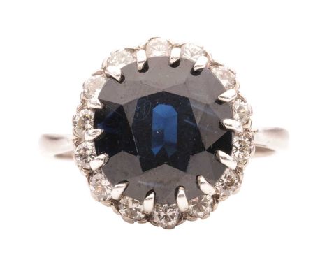 A sapphire and diamond halo ring in 18ct white gold, centred with a circular-cut sapphire of dark blue colour, approximately 