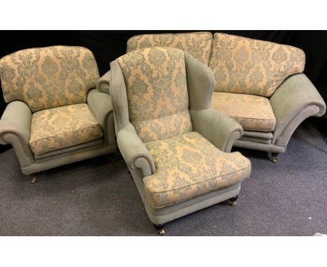 A three seater scroll arm sofa, turned legs, brass casters, along with a conforming wing-back arm chair, and an arm chair, (3