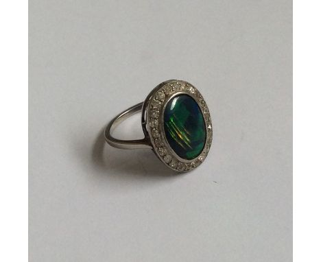 An attractive black opal and diamond oval cluster ring in stylish mount, the opal measuring approx. 12.5 mms long. Est. £500 