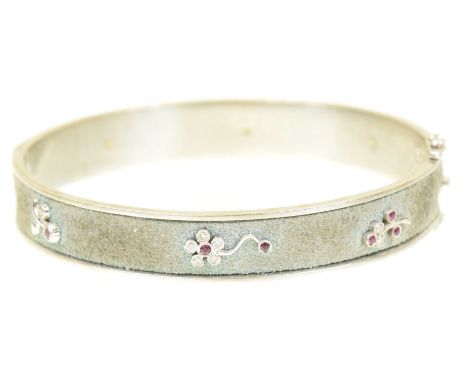 A diamond and ruby hinged bangleThe hinged bangle with blue suede backing and brilliant cut diamond and circular shaped colou