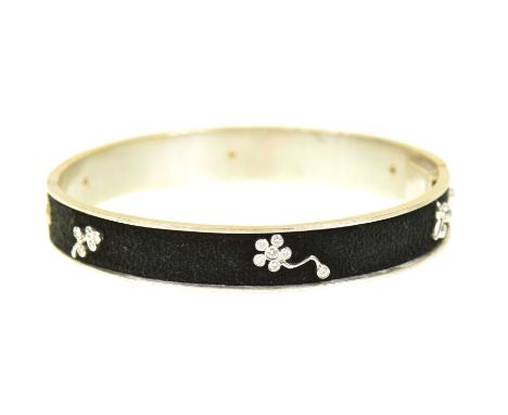 A diamond hinged bangleThe hinged bangle with black suede backing and brilliant cut diamond and colourless gem floral motifs,
