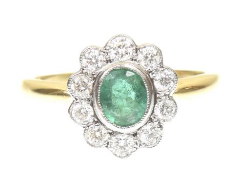 An emerald and diamond cluster ringThe oval shape emerald within a brilliant cut diamond scalloped surround, stamped 18ct, es