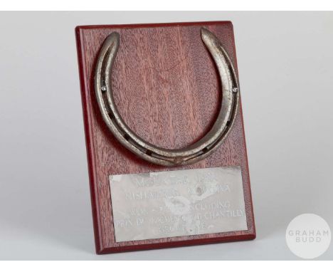 Shoe worn by the racehorse Mouktar,mounted on a wooden plaque with easel support and set with an engraved metal plaque, 20 by