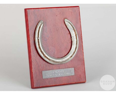 Shoe worn by the racehorse Kalanisi,mounted on a wooden plaque with easel support and set with engraved metal plaque, 20 by 1