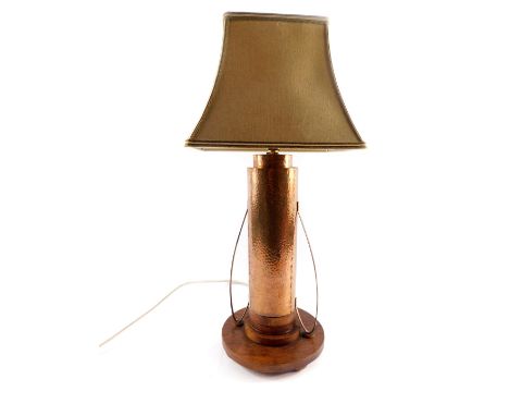 An Art Deco copper table lamp, of hammered double cylindrical form, with scroll arms, raised on a stepped oak circular base, 