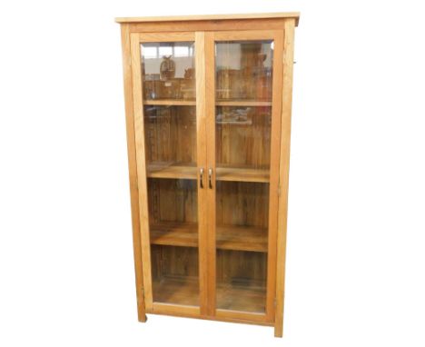 A light oak display cabinet, with a plain pediment over two bevelled glass inset doors, opening to reveal four shelves, raise