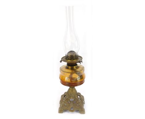 An early 20thC brass oil lamp, the amber glass reservoir on a dulled finish brass base, with chimney, 56cm high.