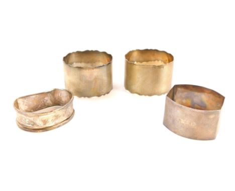 Four silver napkin rings, comprising a pair of George V engine turned decorated napkin rings, one with crest 31-1-56, another