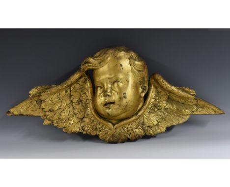 A Continental giltwood architectural cresting, carved as a winged putto mask, 69cm wide, 18th century