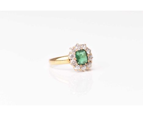 An emerald and diamond cluster ring, designed as a central cushion cut emerald claw set within a border of ten old cut diamon