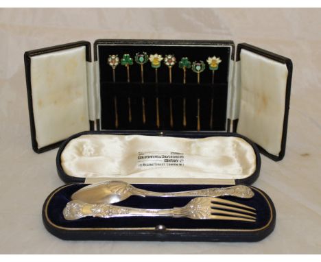 A cased Victorian silver knife and fork set (London 1895), together with a cased set of white metal enamelled cocktail sticks