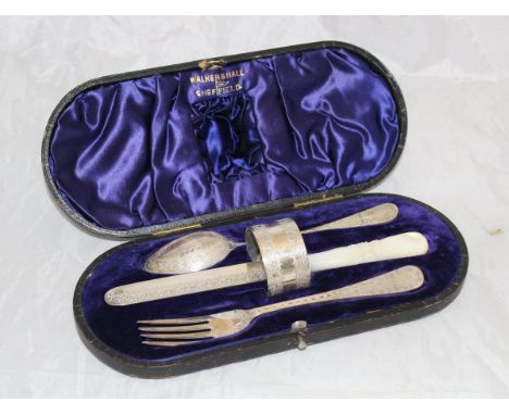 An Edwardian silver cased Christening set comprising knife, fork, spoon and napkin ring (by  Walker & Hall Sheffield 1906) to