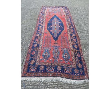 Persian wool carpet, geometric medallions in light and dark blue against a red ground within a blue border, 388 x 152.5cm