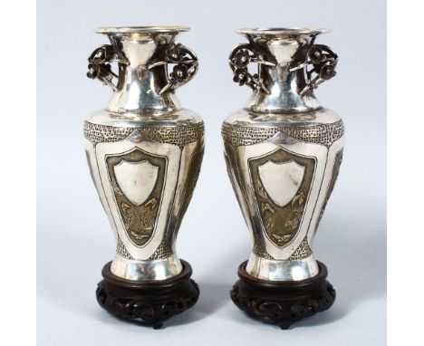 A PAIR OF CHINESE SILVER &amp; SILVER GILT VASES ON HARDWOOD STANDS, the vases each with panels depicting scenes of native fl
