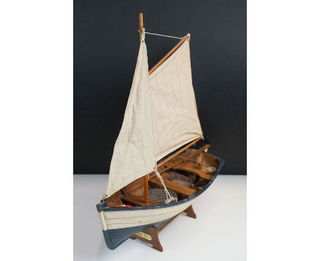 Painted wooden model boat on stand, complete with two sails, pair of oars, fishing net, lobster pot and life ring, 45cm long