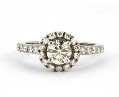 A white metal (tested 18ct gold) halo ring set with an 0.70ct centre diamond surrounded by brilliant cut diamonds, (O.5).