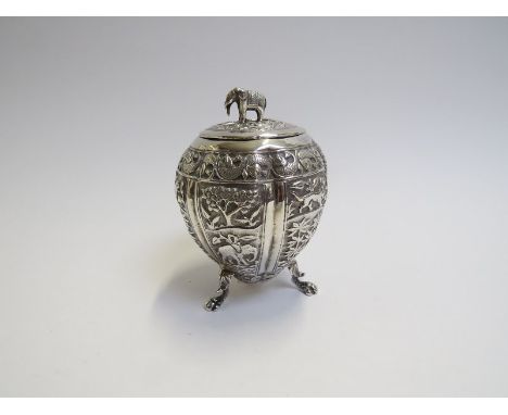 An Indian white metal tea caddy of lobed gourd shape, raised upon three hairy paw feet, the whole repoussé with panels of nat