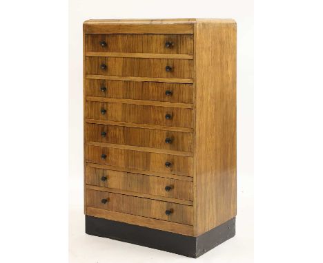 An Art Deco walnut chest of drawers,the cushion top over eight drawers, with Bakelite button handles, on an ebonised plinth, 