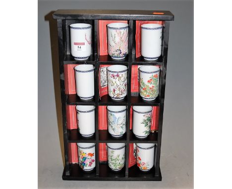 A set of twelve Japanese porcelain beakers, each enamel decorated with flowers and foliage, in ebonised stand