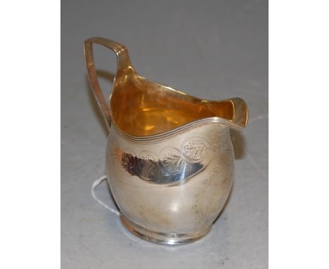 A George III silver helmet shaped cream jug, having a gilt wash interior and floral engraved outer decoration with vacant car