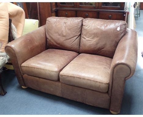 A LEATHER UPHOLSTERED TWO-SEATER SOFA with aged effect upholstery, on bun feet 150cm wide, 96cm deep